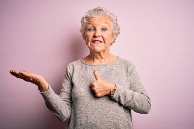 Senior beautiful woman wearing casual t-shirt standing over isolated pink background Showing palm hand and doing ok gesture with thumbs up, smiling happy and cheerful