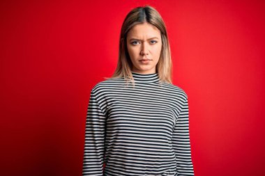 Young beautiful blonde woman wearing casual striped sweater over red isolated background skeptic and nervous, frowning upset because of problem. Negative person.