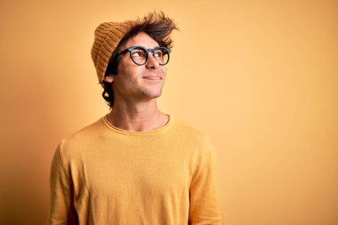 Young handsome man wearing casual t-shirt and glasses over isolated yellow background smiling looking to the side and staring away thinking.