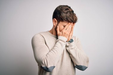 Young handsome blond man with beard and blue eyes wearing casual sweater with sad expression covering face with hands while crying. Depression concept.