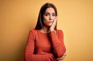 Young beautiful brunette woman wearing casual t-shirt standing over yellow background thinking looking tired and bored with depression problems with crossed arms.