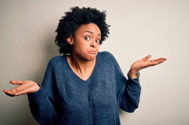 Kıvırcık saçlı, sıradan bir süveter giyen, elleri ve kolları havada, kafası karışmış genç ve güzel Afro-Amerikan bir kadın. Şüphe kavramı.