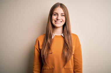 Genç, güzel, kızıl saçlı bir kadın izole edilmiş beyaz arka plan üzerine sıradan bir süveter giyiyor. Yüzünde mutlu ve havalı bir gülümseme var. Şanslı kişi..