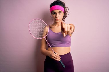 Kıvırcık saçlı, spor giyinen, badminton oynayan, kamerayı işaret eden güzel bir sporcu kadın ve sen, el işareti, ön taraftan pozitif ve kendinden emin bir jest.
