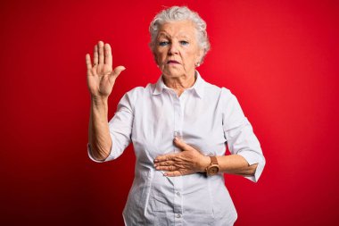 Senior beautiful woman wearing elegant shirt standing over isolated red background Swearing with hand on chest and open palm, making a loyalty promise oath