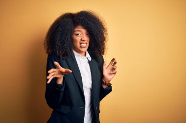 Young beautiful african american business woman with afro hair wearing elegant jacket disgusted expression, displeased and fearful doing disgust face because aversion reaction. With hands raised