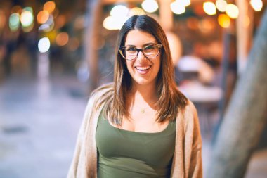 Mutlu ve kendinden emin gülümseyen genç ve güzel bir kadın. Kasaba caddesinde yüzünde gülümsemeyle dikilirken