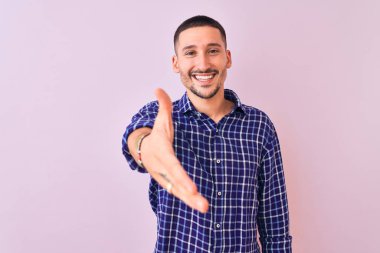 Soyutlanmış arka planda duran yakışıklı genç adam dostça bir selamlama ve hoş geldin hediyesi olarak el sıkışmayı sunuyor. Başarılı bir iş..