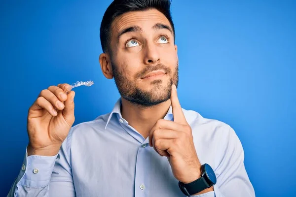 Jovem Homem Bonito Segurando Dente Aligner Correção Sobre Fundo Azul — Fotografia de Stock