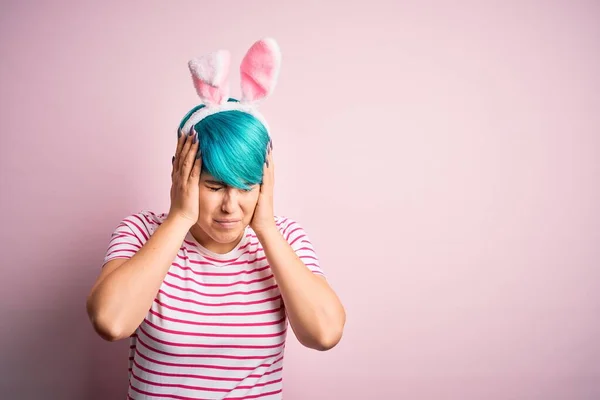 由于疼痛和偏头痛 年轻的女人有着时尚的蓝色头发 带着东方兔子的耳朵 背景是粉色的 极度头痛和紧张 手放在头上 — 图库照片
