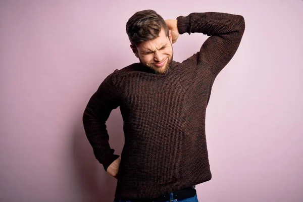 Young blond man with beard and blue eyes wearing casual sweater over pink background stretching back, tired and relaxed, sleepy and yawning for early morning