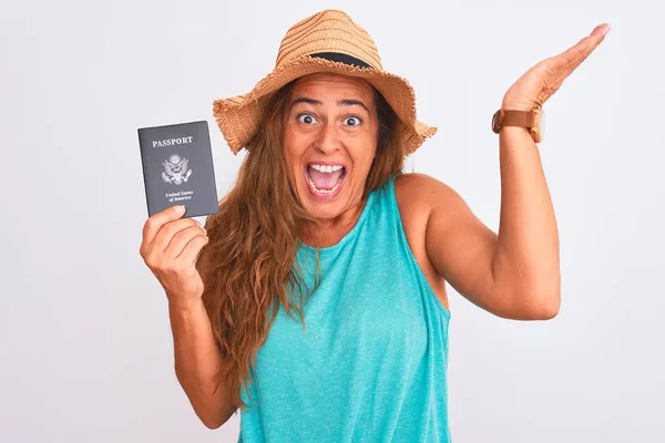孤立した背景の上に米国のパスポートを保持している中年の成熟した観光客の女性は非常に幸せと興奮 大きな笑顔で叫んで勝利を祝う勝者の式と手を上げ — ストック写真