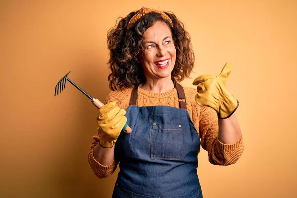 Gärtnerin Mittleren Alters Trägt Schürze Mit Harke Über Gelbem Hintergrund — Stockfoto