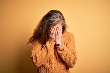 Sarı arka planda dikilen gündelik süveter giyen genç ve güzel sarışın bir kadın. Ağlarken yüzünü ellerle kapatan üzgün bir ifade. Depresyon kavramı.