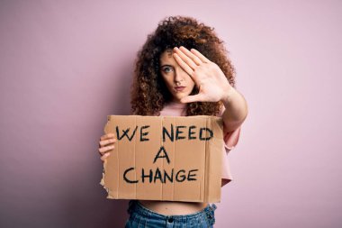 Kıvırcık saçlı ve piercingli genç ve güzel bir kadın. Değişiklik istiyor, eli açık, dur işareti yapıyor, ciddi ve kendinden emin bir ifadeyle savunma yapıyor.