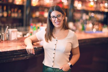 Mutlu ve kendinden emin gülümseyen genç ve güzel bir kadın. Yüzünde gülümsemeyle restorandaki tezgah demirine yaslanarak duruyorum.