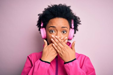 Kıvırcık saçlı, pembe kulaklık takmış, müzik dinleyen Afro-Amerikalı genç bir kadın ağzını yanlışlıkla elleriyle kapatmış. Gizli konsept.
