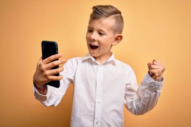 Küçük beyaz bir çocuk akıllı telefon kullanıyor ve telefonun ekranına bakıp gururla bağırıyor zaferi ve başarıyı kutluyor çok heyecanlı, coşkulu bir duygu.