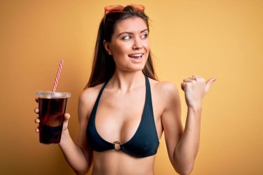 Tatilde mavi gözlü, bikinili, kola içen genç ve güzel bir kadın.