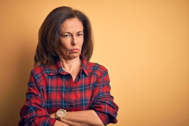 Middle age beautiful woman wearing casual shirt standing over isolated yellow background skeptic and nervous, disapproving expression on face with crossed arms. Negative person. clipart