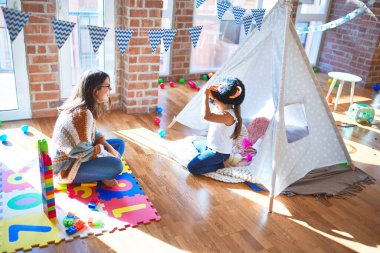 Anaokulunda bir sürü oyuncağın etrafında maymun maskesiyle oynayan güzel öğretmen ve bebek.