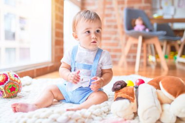 Anaokulunda battaniyenin üzerinde bir sürü oyuncağın etrafında oturan güzel çocuk.