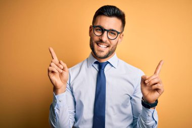Sarı arka planda duran kravat ve gözlük takan genç yakışıklı işadamı farklı yönleri gösteren kendine güvenle gülümsüyor. Reklam için boşluk kopyala