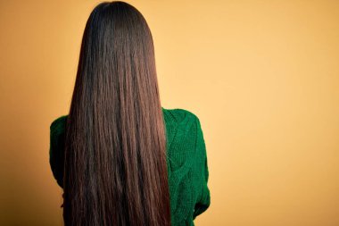 Sarıya boyanmış yeşil süveter giyen genç, güzel Asyalı kadın geriye dönüp kollarını kavuşturmuş bakıyor.