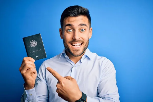 持澳大利亚护照的年轻英俊游客带着蓝色背景的证件 很高兴用手和手指指指点点 — 图库照片