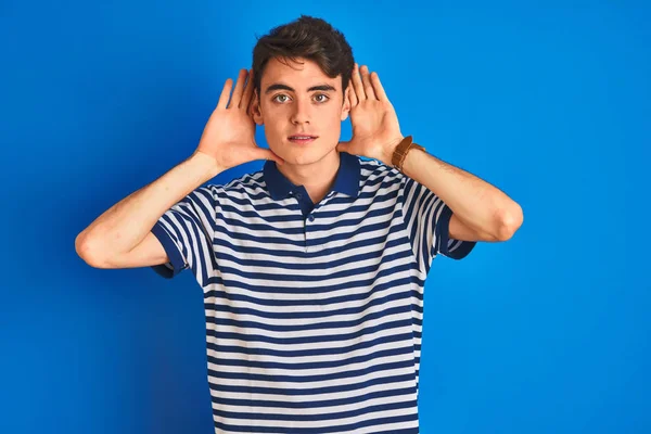 青い隔離された背景の上に立ってカジュアルなTシャツを着て10代の少年耳のジェスチャーで両方の手を聞くしようとすると ゴシップへの好奇心 聴覚障害 聴覚障害 — ストック写真
