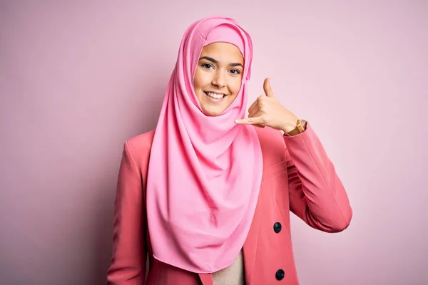 孤立したピンクの背景の上に立つイスラム教徒のヒジャーブを身に着けている若い美しい少女は 電話で話すような手や指で電話のジェスチャーをして笑っています 概念の伝達 — ストック写真