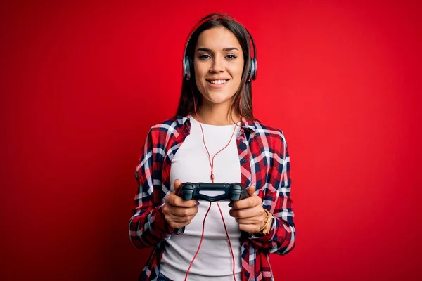 年轻美丽的黑发游戏女玩家用操纵杆和耳机玩电子游戏 脸上挂着快乐的表情 脸上挂着自信的微笑 露出牙齿 — 图库照片