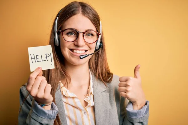 Young redhead call center agent woman overworked using headset holding help remidner happy with big smile doing ok sign, thumb up with fingers, excellent sign