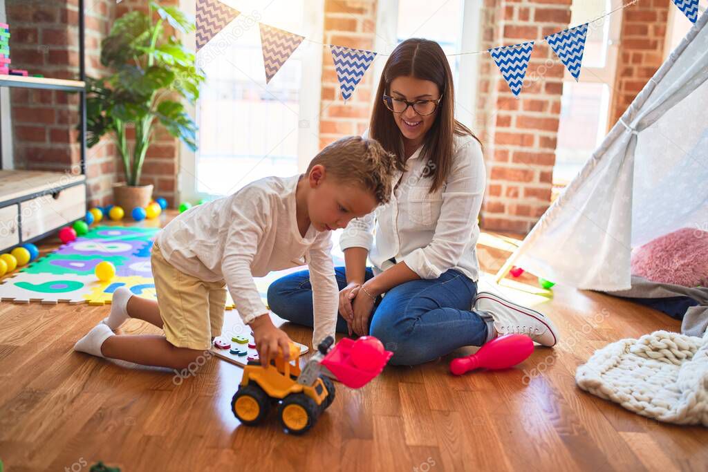 Beautiful teacher and toddler playing with tractor around lots of toys at kindergarten