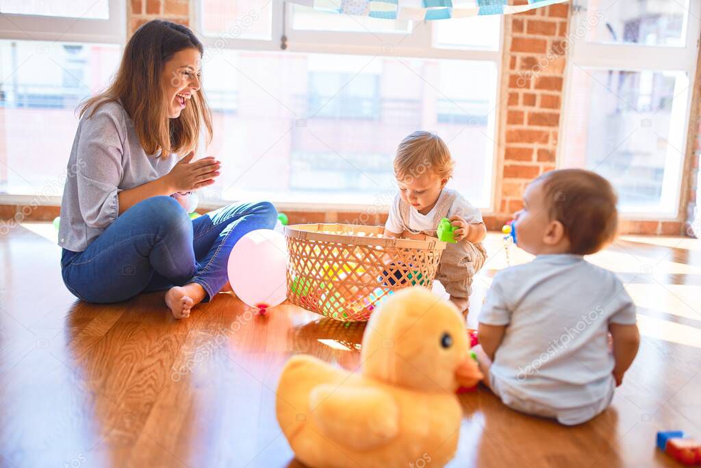 Beautiful teacher and toddlers playing around lots of toys at kindergarten