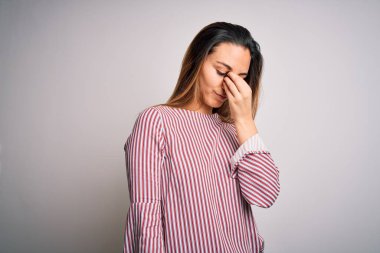 Mavi gözlü, beyaz arka planda dikişli tişört giyen genç, güzel sarışın kadın yorgun burnu ve gözleri ovuşturarak yorgunluk ve baş ağrısı hissediyor. Stres ve hüsran kavramı.