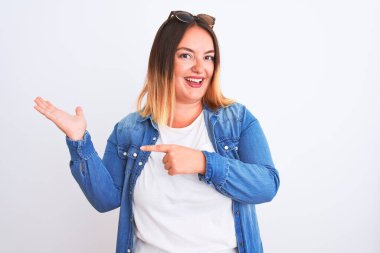 İzole edilmiş beyaz arka planda duran kot gömlek giyen güzel bir kadın kameraya hayret ediyor ve gülümsüyor..