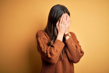 İzole edilmiş sarı arka plan üzerinde duran sıradan bir süveter giyen genç ve güzel bir kız. Ağlarken yüzünü ellerle kapatan üzgün bir yüz ifadesi. Depresyon kavramı.