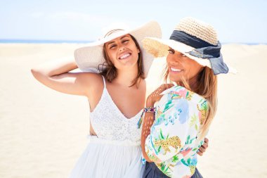 Şapka ve yaz kıyafetleri içinde mutlu ve kendinden emin gülümseyen genç ve güzel arkadaşlar. Yüzünde bir gülümsemeyle sahilde dikilirken
