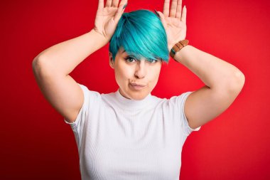 Mavi saçlı, kırmızı arka planda günlük tişört giyen, avuçlarında alaycı ve şüpheci ellerle tavşan kulağı hareketi yapan genç ve güzel bir kadın. Paskalya tavşanı kavramı.