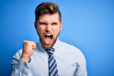 Sarışın, sakallı, mavi gözlü, şık gömlekli ve kravatlı genç bir işadamı kızgın ve kızgın duruyor. Öfkeyle bağırırken yumruğunu kaldırıyor. Öfke ve agresif kavram.