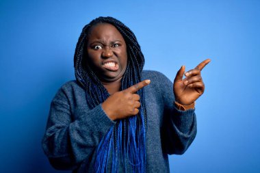 Mavi arka planda günlük süveter giyen Afrikalı Amerikalı artı cüsseli bir kadın endişeli ve gergin bir tarafa, endişeli ve şaşırmış bir ifade takınıyor.