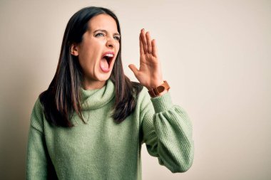 Mavi gözlü, beyaz arka planda balıkçı yaka kazak giyen, elleri ağızda bağırarak ve yüksek sesle bağıran genç esmer kadın. İletişim konsepti.