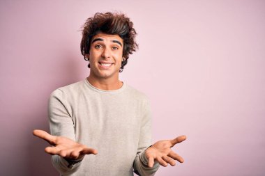 İzole edilmiş pembe arka planda duran, rahat bir tişört giyen yakışıklı genç adam, güler yüzlü, güler yüzlü, dostça bir karşılama, olumlu ve kendinden emin bir selamlama olarak.