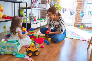 Güzel öğretmen kadın ve bebek anaokulunda bir sürü oyuncağın etrafında taşlarla oynuyorlar.