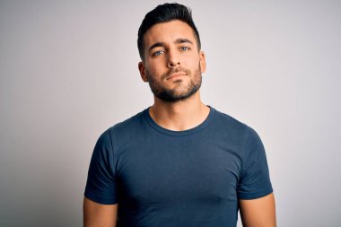 İzole edilmiş beyaz arka planda duran sıradan tişört giyen yakışıklı genç adam yüzünde ciddi bir ifadeyle rahatlamış. Basit ve doğal bir şekilde kameraya bakıyorsun..