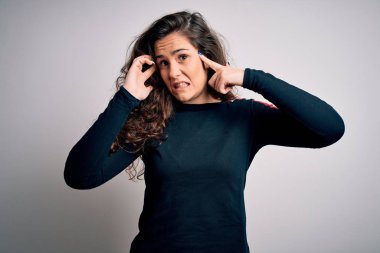 Kıvırcık saçlı genç bir kadın izole edilmiş beyaz arka plan üzerine günlük süveter giyip yüksek sesli müzik sesi için kulakları parmaklarıyla kapatıyor. Sağır kavramı.