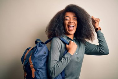 Afro saçlı, sırt çantalı, gururla bağıran, zaferi ve başarıyı kutlayan heyecanlı, coşkulu, neşe dolu genç Afro-Amerikan öğrenci kadın.