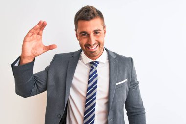 Takım elbiseli ve kravatlı genç yakışıklı iş adamı izole edilmiş arka planda gülümsüyor ve kendine güvenen el hareketleriyle küçük beden işareti yapıyor parmaklarıyla ve kamerayla bakıyor. Ölçü kavramı.