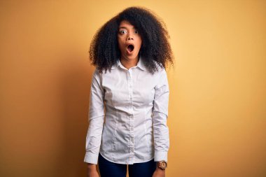 Afro saçlı, sarı arka planda duran güzel Afro-Amerikan zarif genç kadın şaşkınlık ve şaşkınlık ifadesi, korku ve heyecan dolu yüz ifadesiyle dehşete düşmüş ve şok olmuştu..